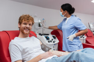Smiling man receiving IV treatment with a nurse checking equipment in the background